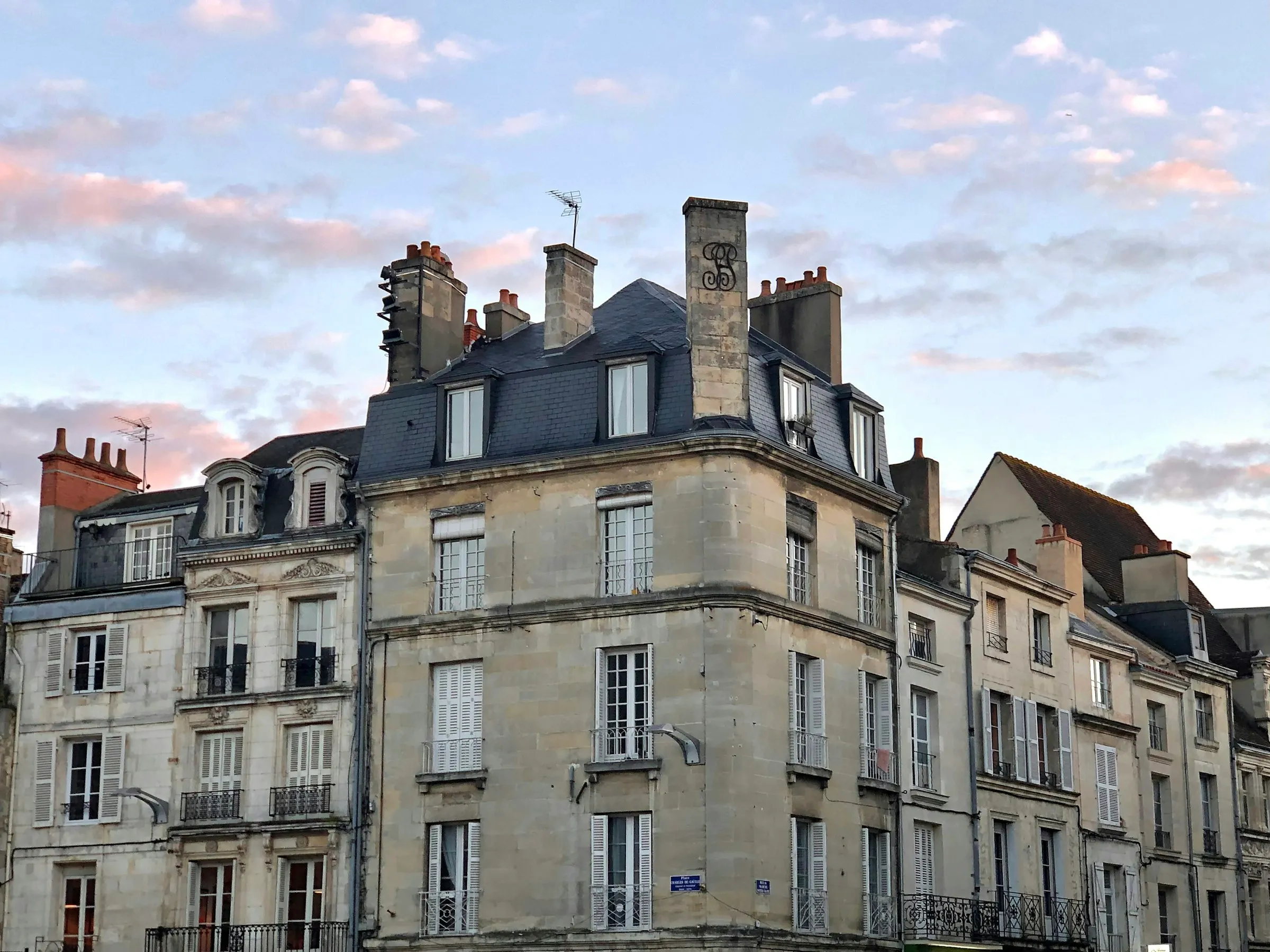 Warm golden-hour light on the pale limestone facades, tall chimneys and slate mansard roofs of the old town around Place Charles de Gaulle in Poitiers.