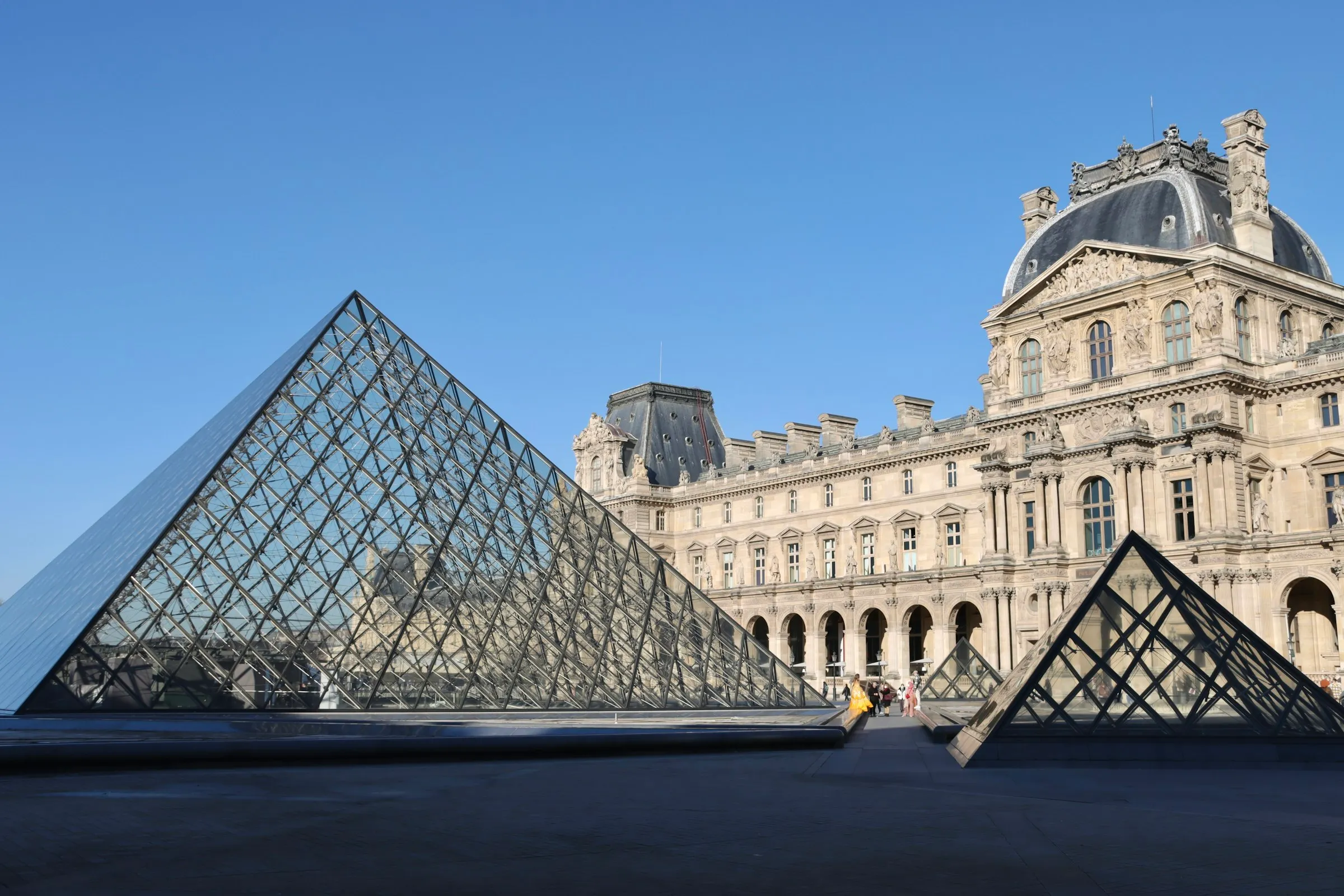 The glass pyramid of the Louvre sparkling under a clear blue sky in the palace's grand courtyard