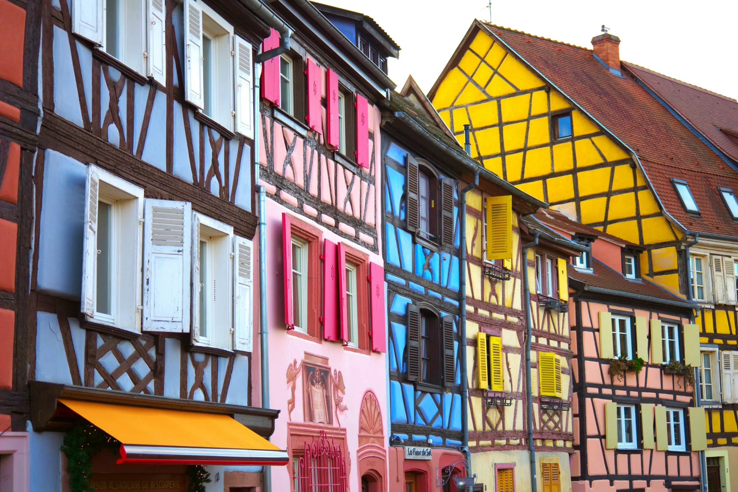 A row of brightly painted half-timbered houses in Colmar old town, blue, pink and yellow facades with carved shutters