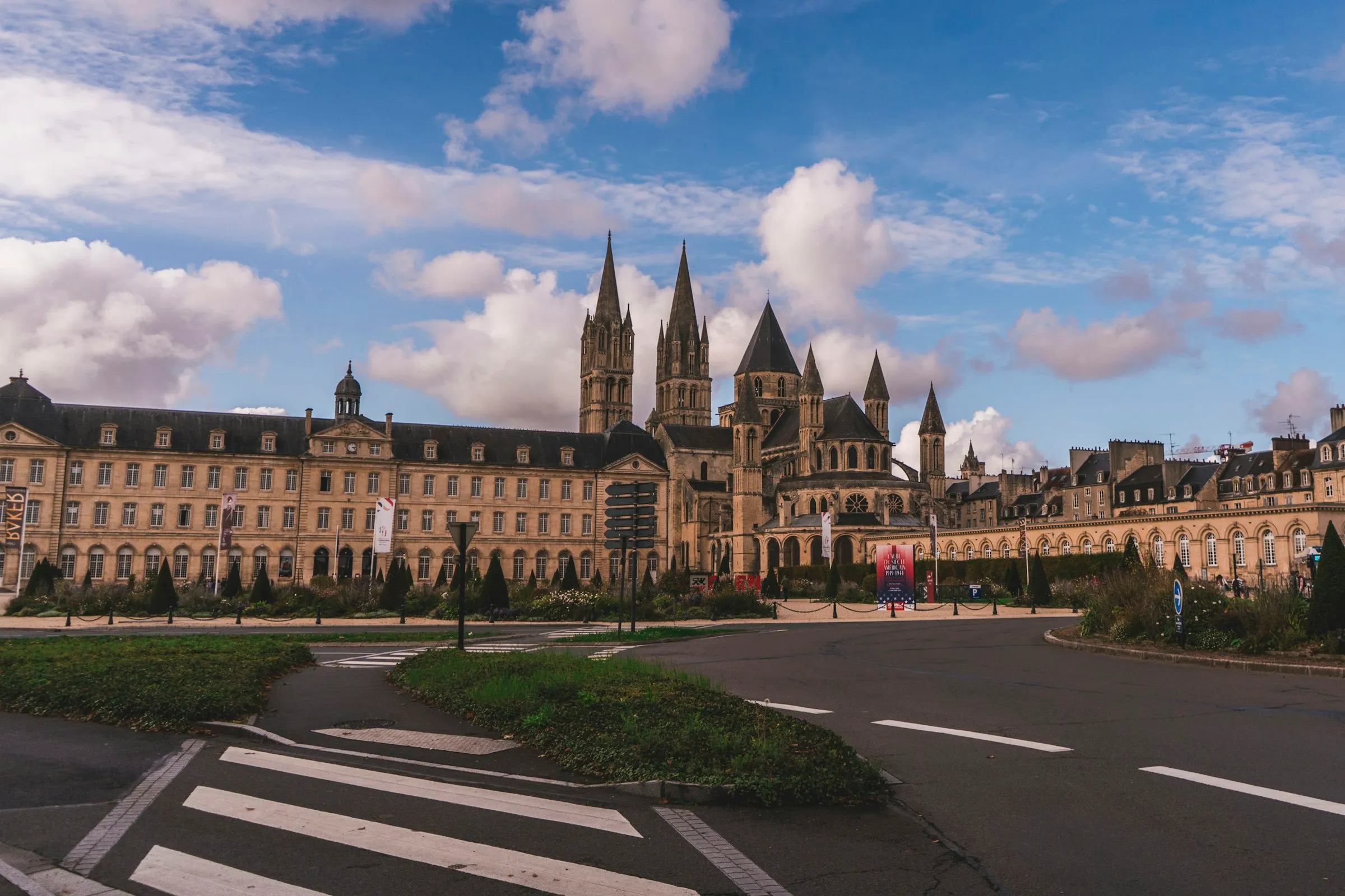 The twin Gothic spires and Romanesque lantern tower of Caen's Abbaye aux Hommes (Saint-Etienne), founded by William the Conqueror, rising above the honey-stone former convent under a bright blue sky