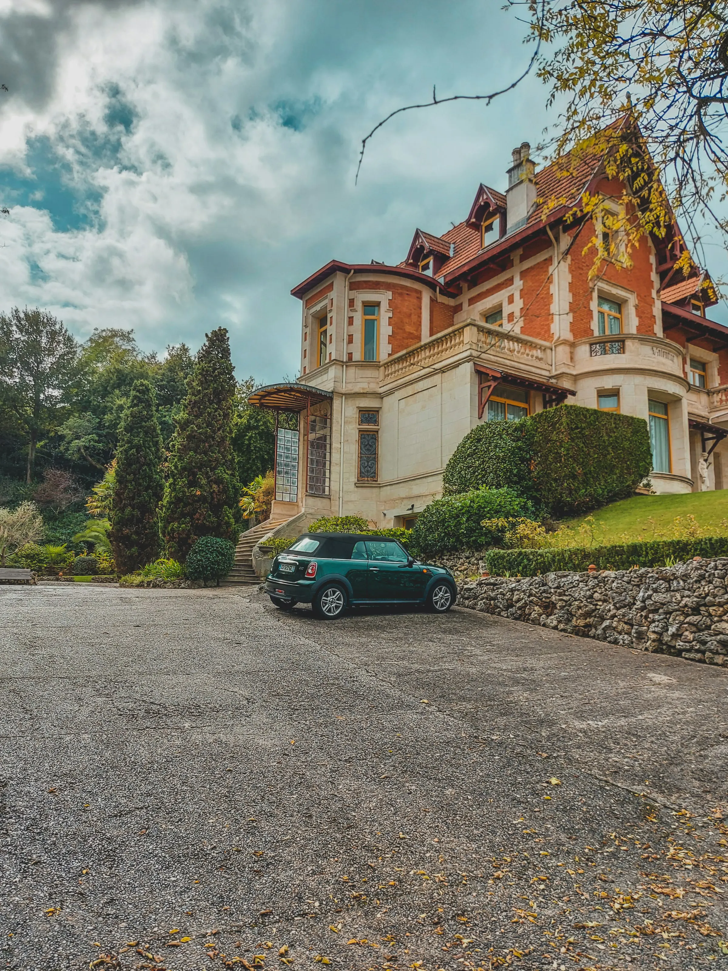 A grand Belle Epoque villa of Arcachon's Ville d'Hiver in red brick and pale stone, with a turret, timber gables and a manicured hedged garden under a dramatic cloudy sky.
