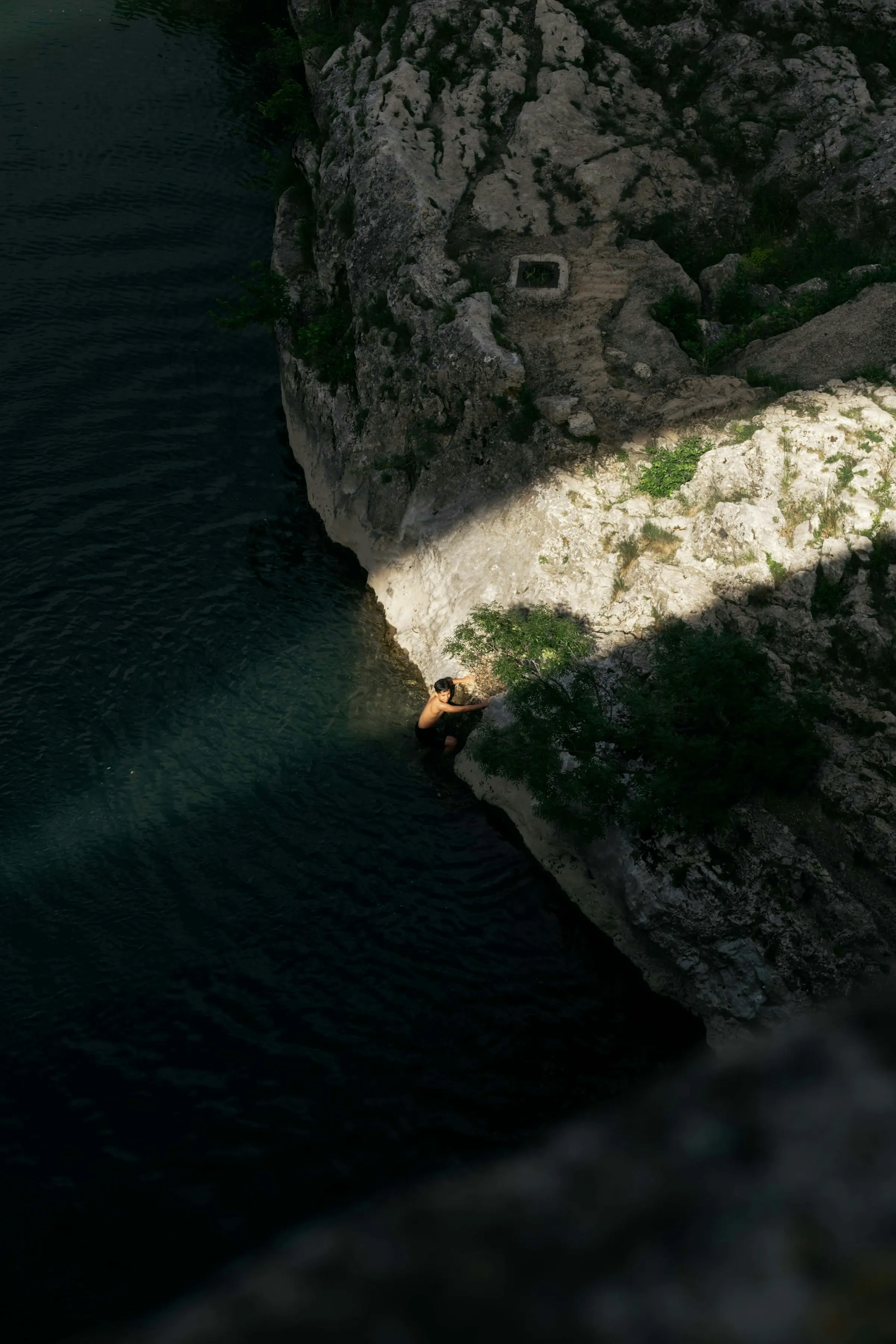 A swimmer in the deep green pool of the Gardon river gorge below pale sunlit limestone cliffs, in the countryside near Uzès