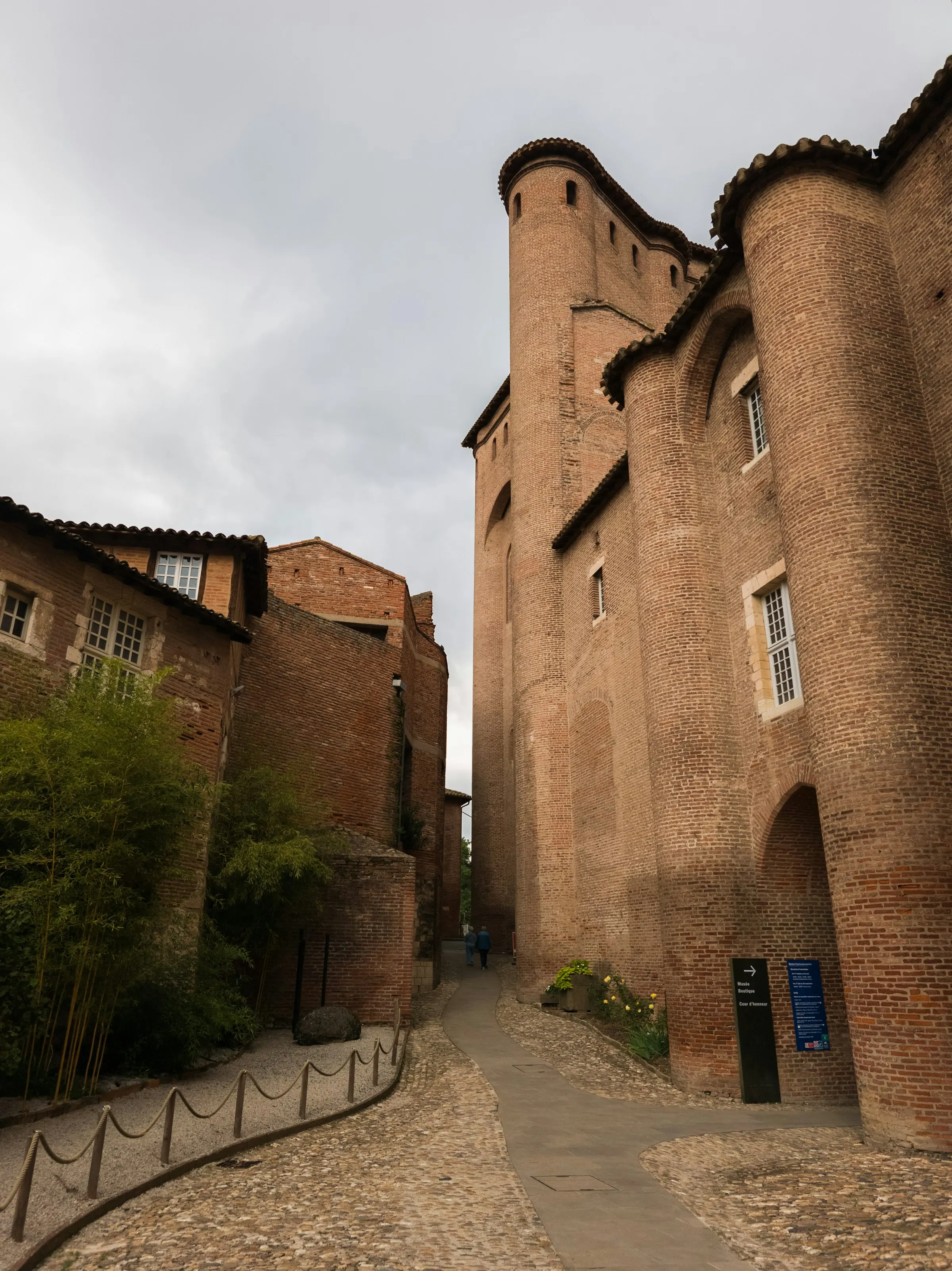 A cobbled lane climbing past the towering red-brick walls and rounded towers of the Palais de la Berbie, home of the Toulouse-Lautrec museum, in Albi's old town.