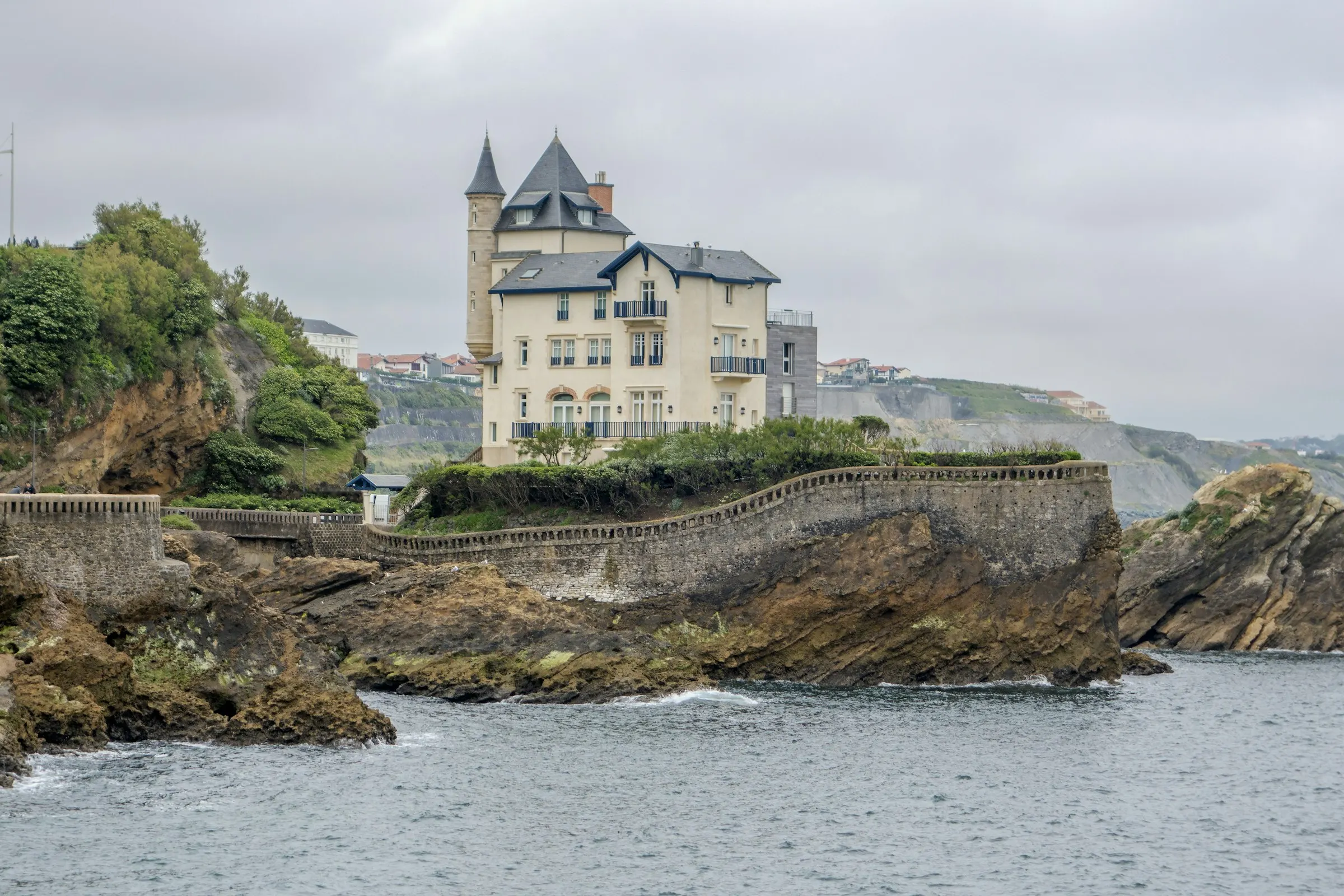 The turreted stone Villa Belza perched on a rocky headland above the Atlantic in Biarritz, with the town's rooftops rising on the hillside behind it