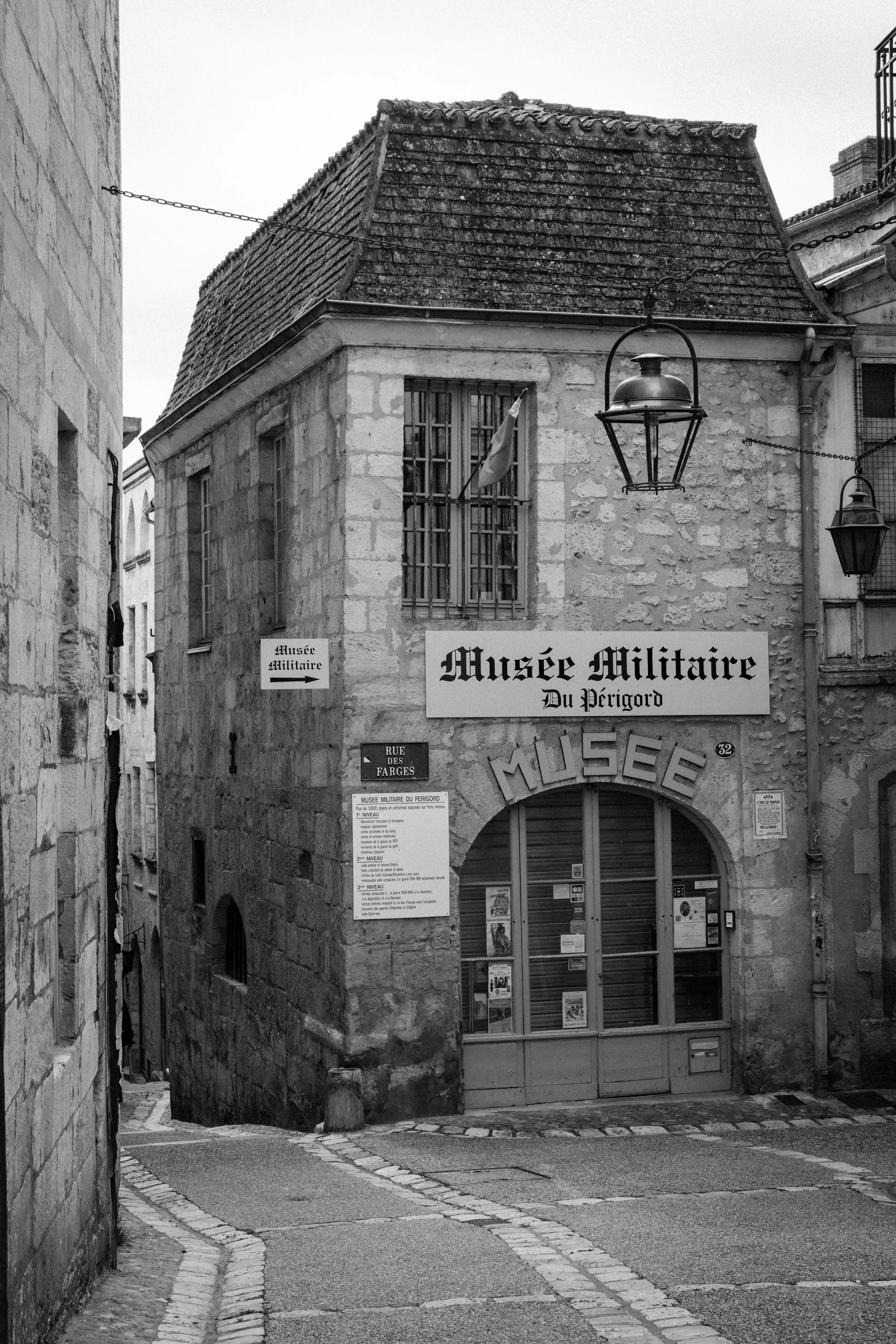 The steep corner of Rue des Farges in Perigueux, where the Musee Militaire du Perigord occupies an old stone house with a weathered tiled roof and an iron lantern