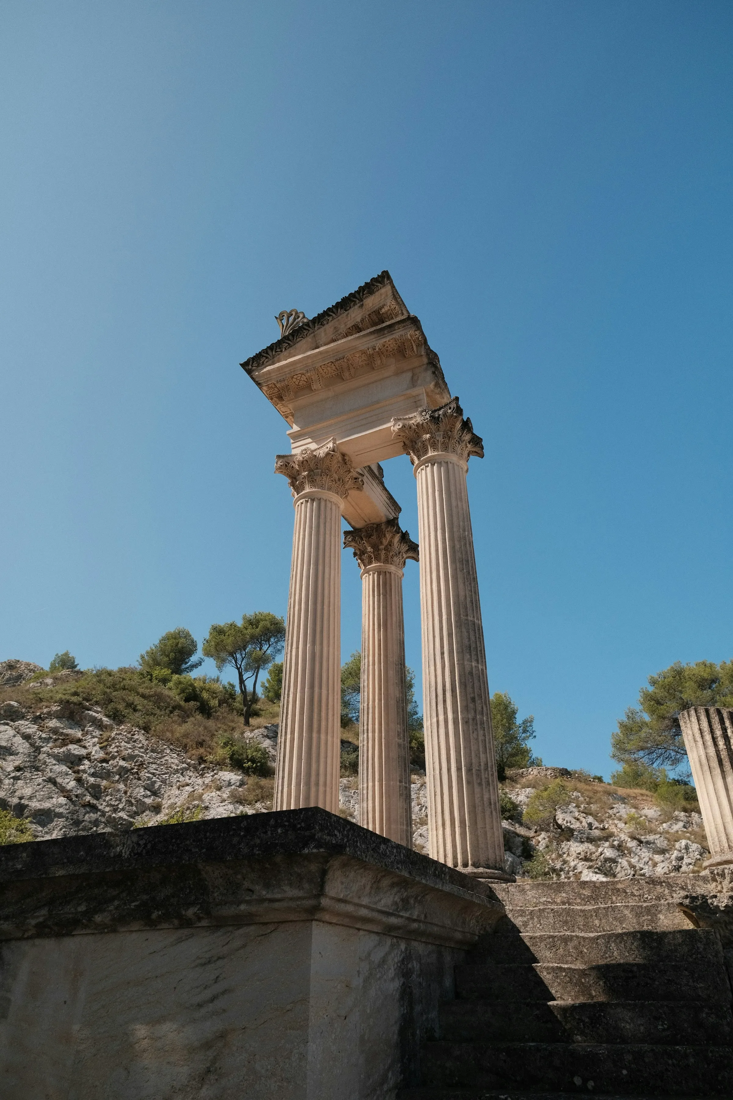 The fluted Corinthian columns of the Roman twin temples at the Glanum archaeological site on the edge of Saint-Remy-de-Provence, glowing pale against a clear blue sky.