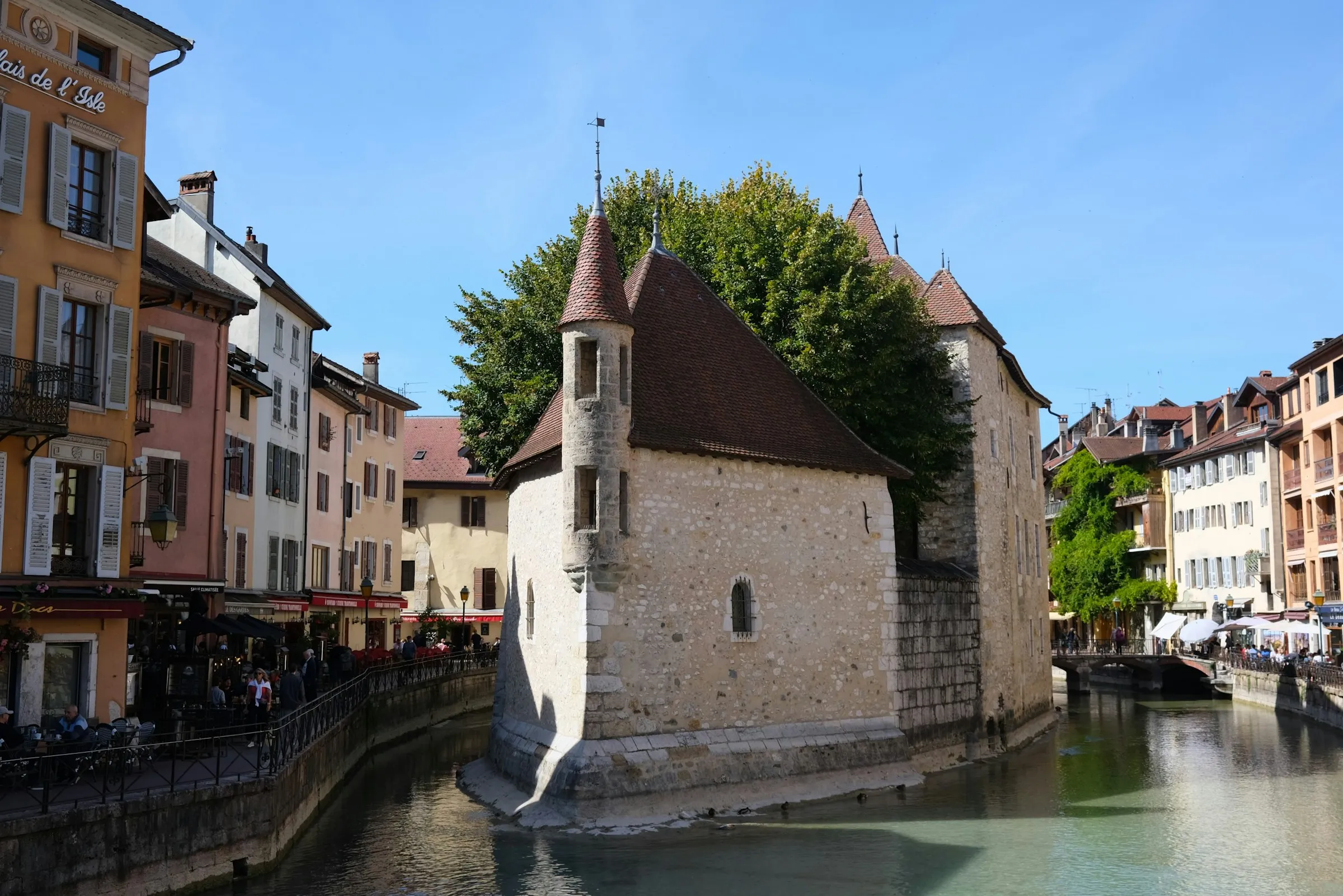 The Palais de l Isle, the medieval island prison on the Thiou canal in Annecy, pastel old-town houses and cafe terraces around it