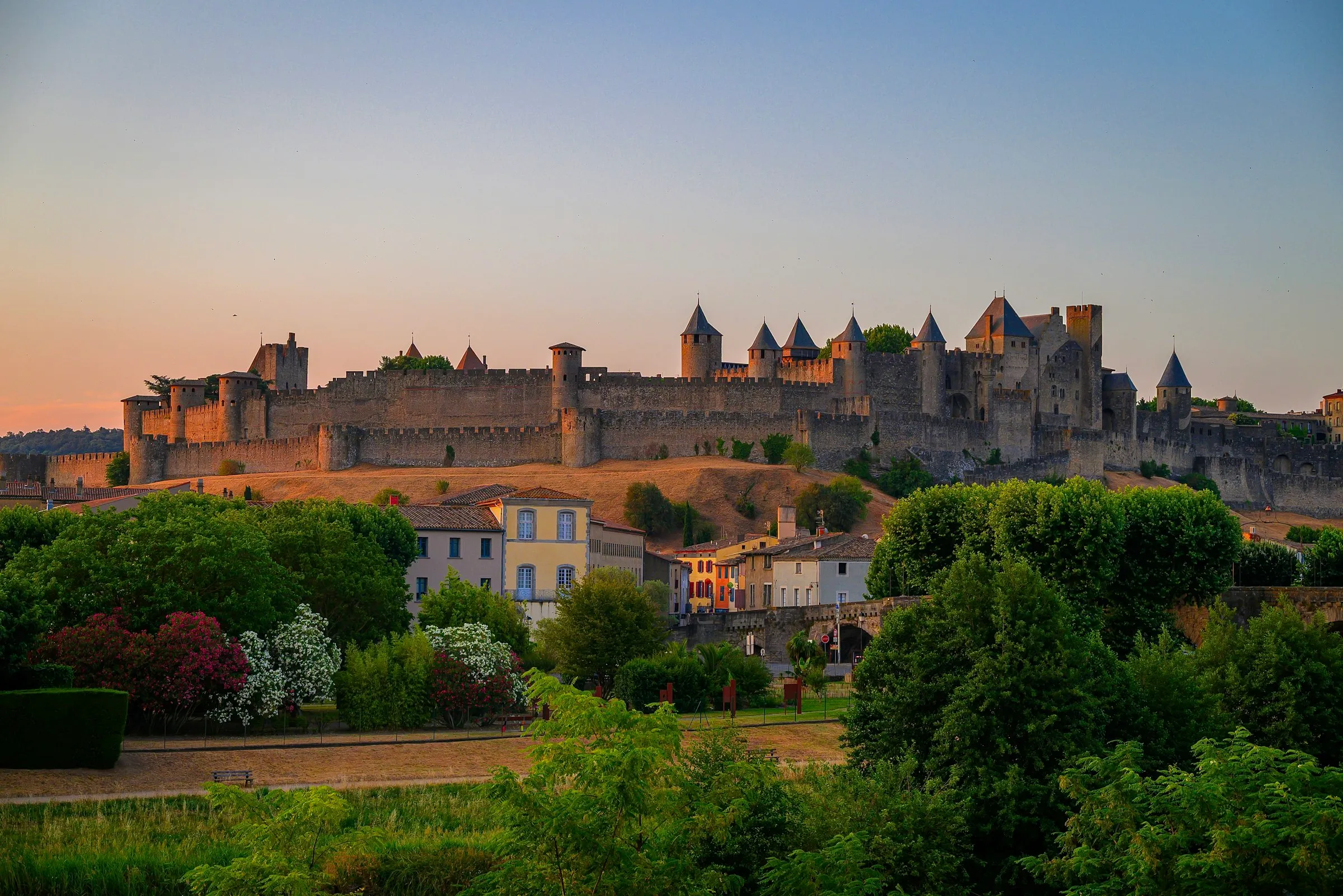Carcassonne's medieval walled city glowing gold at sunset on its hilltop, conical-roofed towers and long ramparts above the lower town