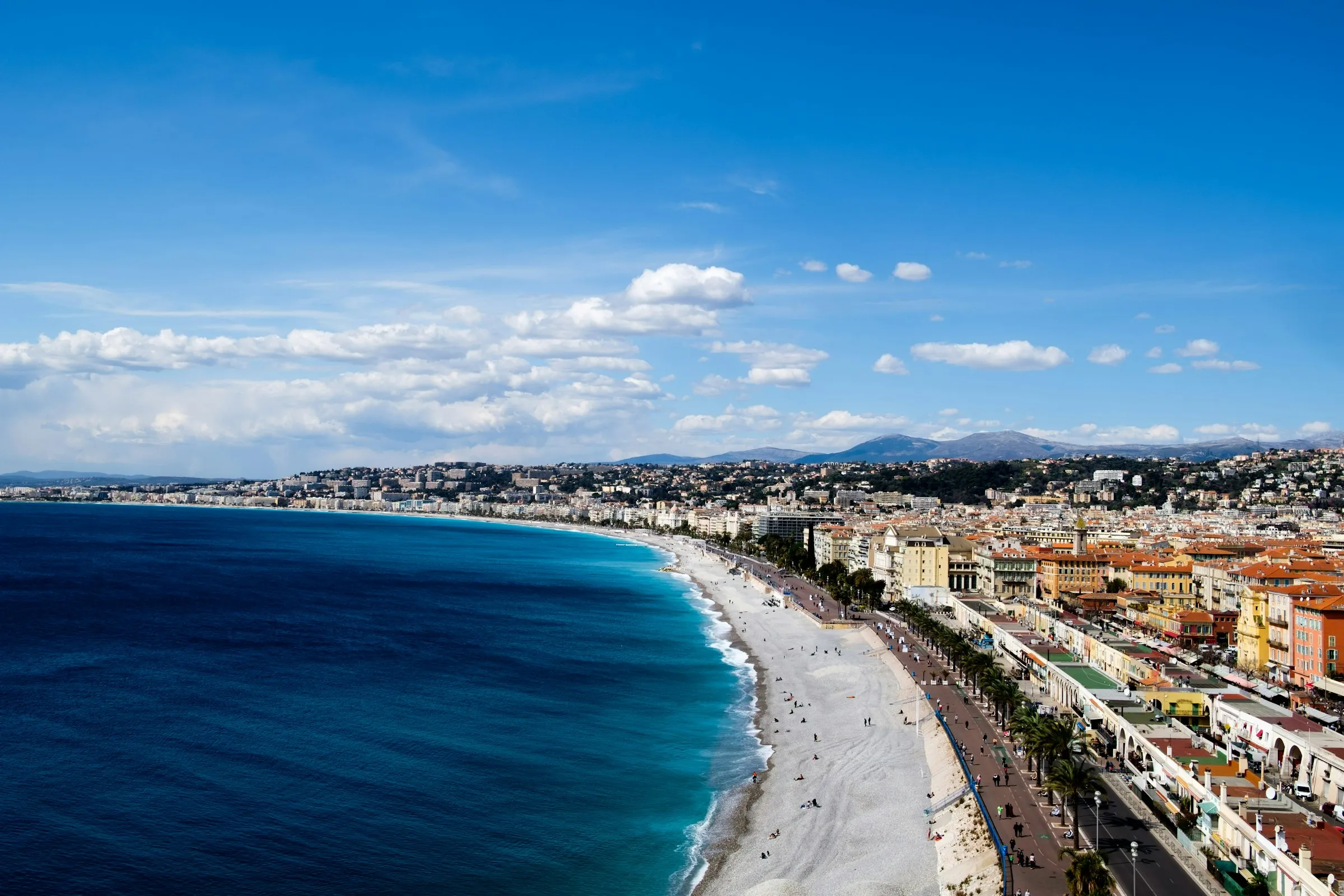 The Baie des Anges in Nice, a curving pebble beach and the palm-lined Promenade des Anglais along a turquoise sea