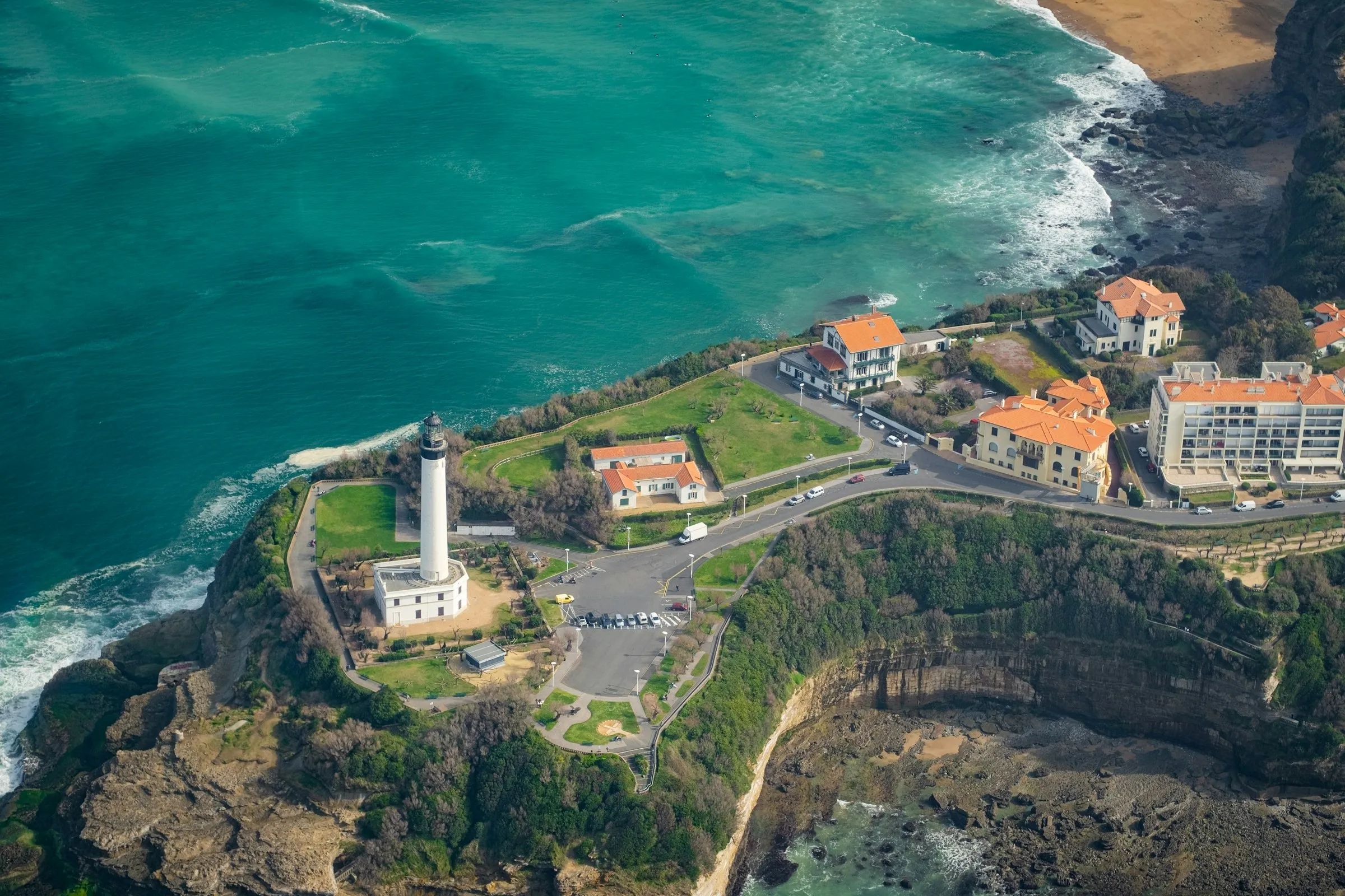 Aerial view of the Pointe Saint-Martin headland in Biarritz, the white Phare lighthouse and belle-epoque villas set above turquoise Atlantic water and a sandy cove