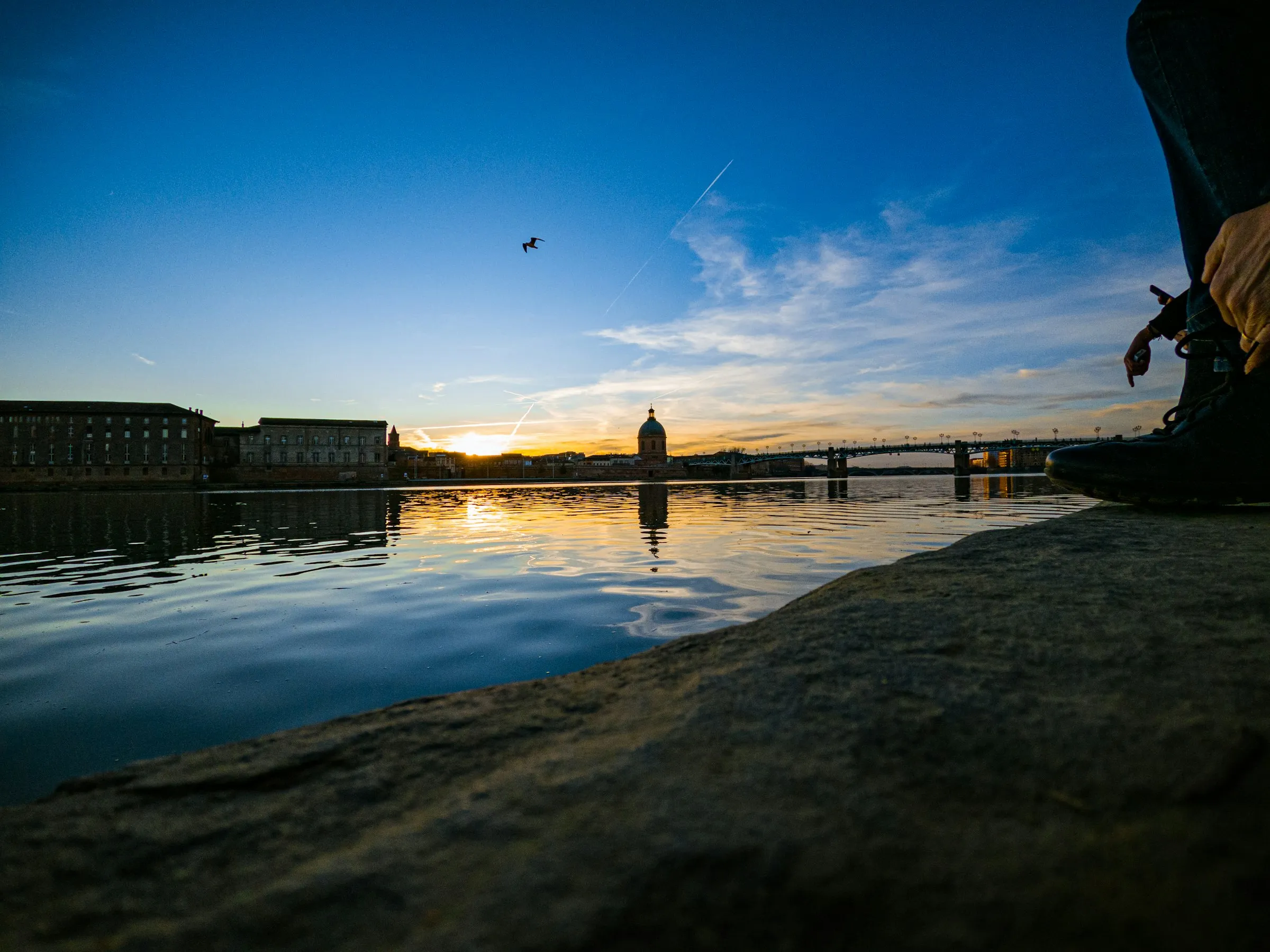 Sunset over the Garonne in Toulouse, the green dome of the Hopital de La Grave and the Pont Saint-Pierre silhouetted against a golden sky with mirror-still reflections on the water.