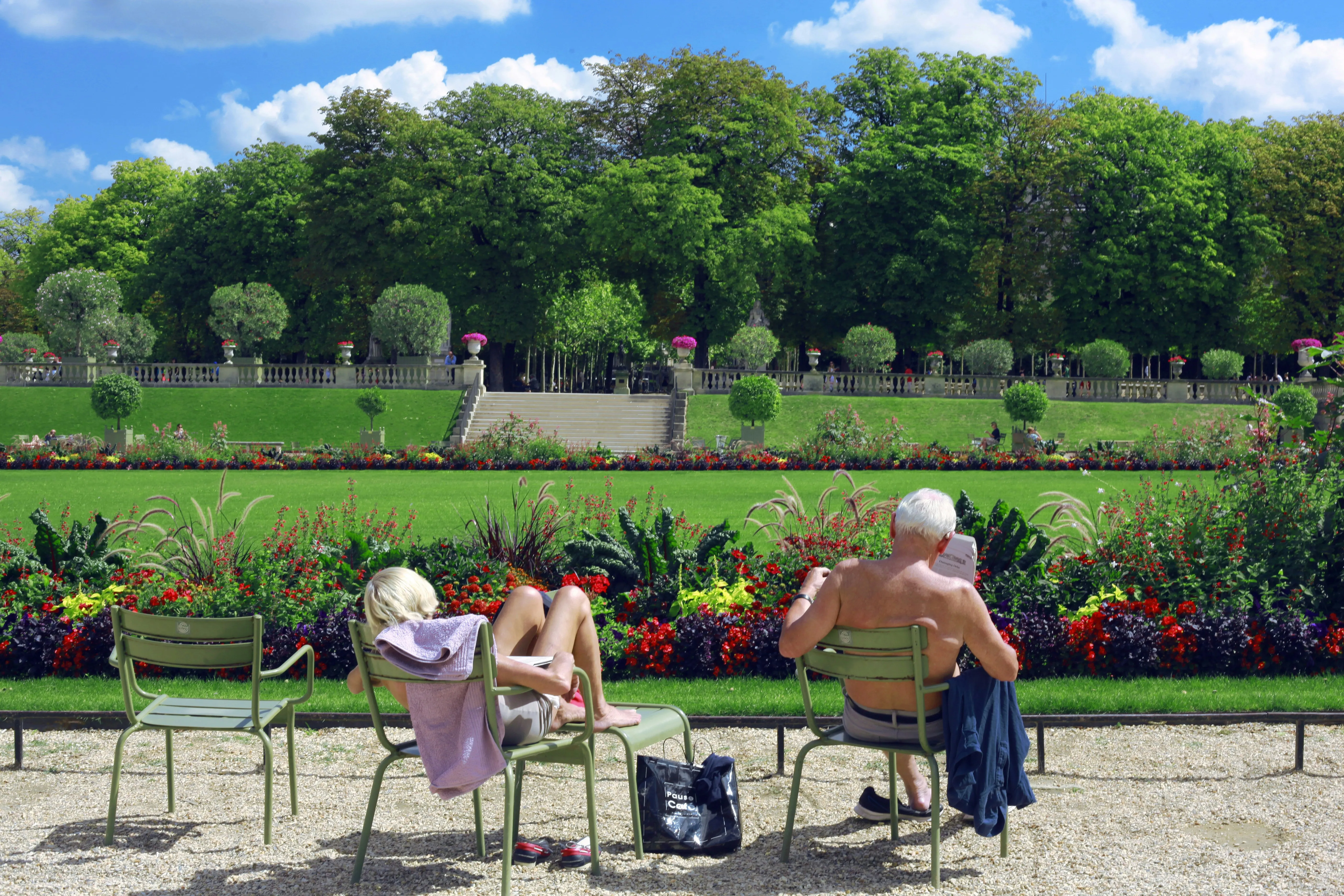 A couple reading on green chairs by the flowerbeds of the Jardin du Luxembourg in Paris