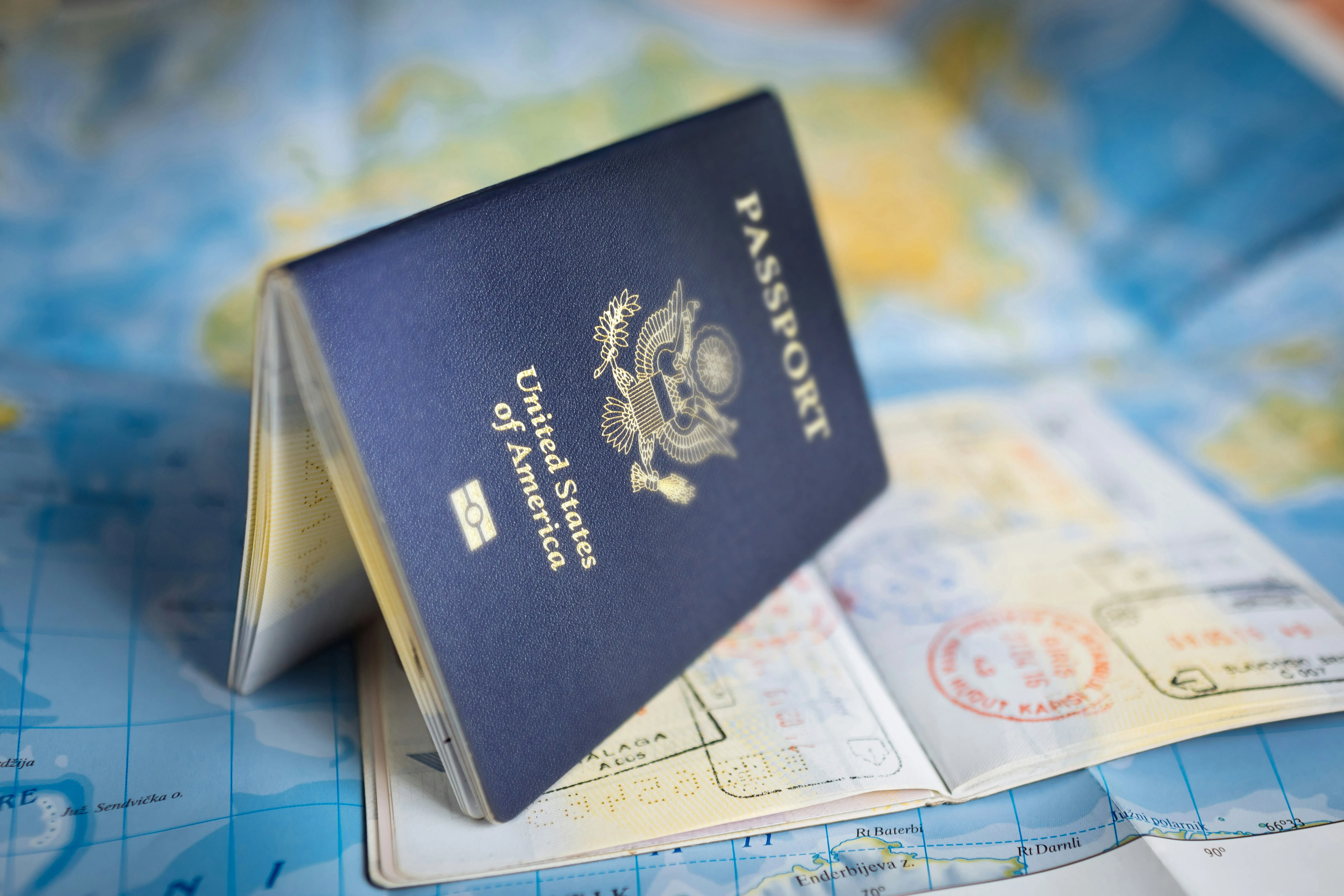 A US passport standing on an open, well-stamped passport over a map of the world