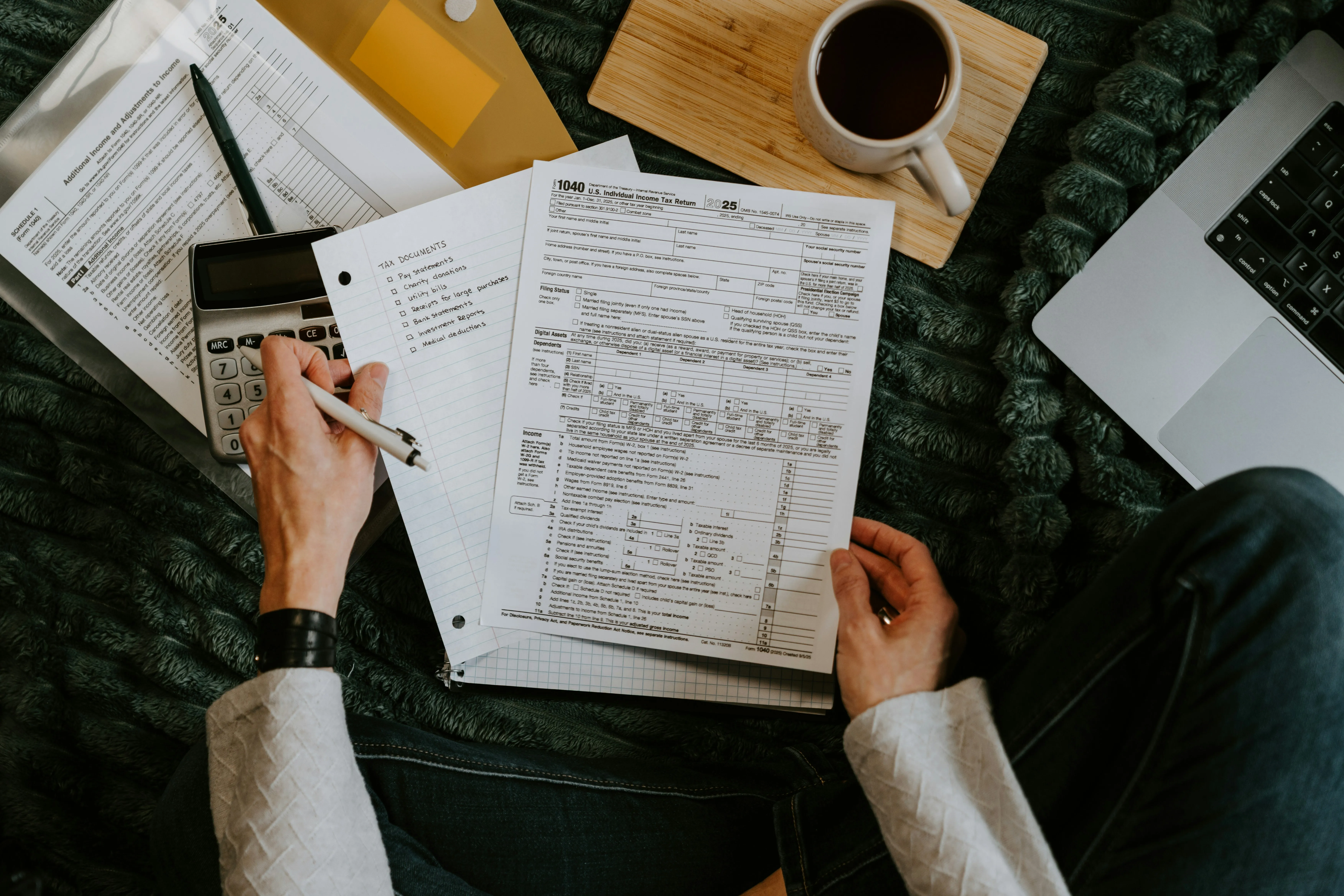 Filling out IRS Form 1040 by hand, with a tax-documents checklist, calculator, and coffee alongside