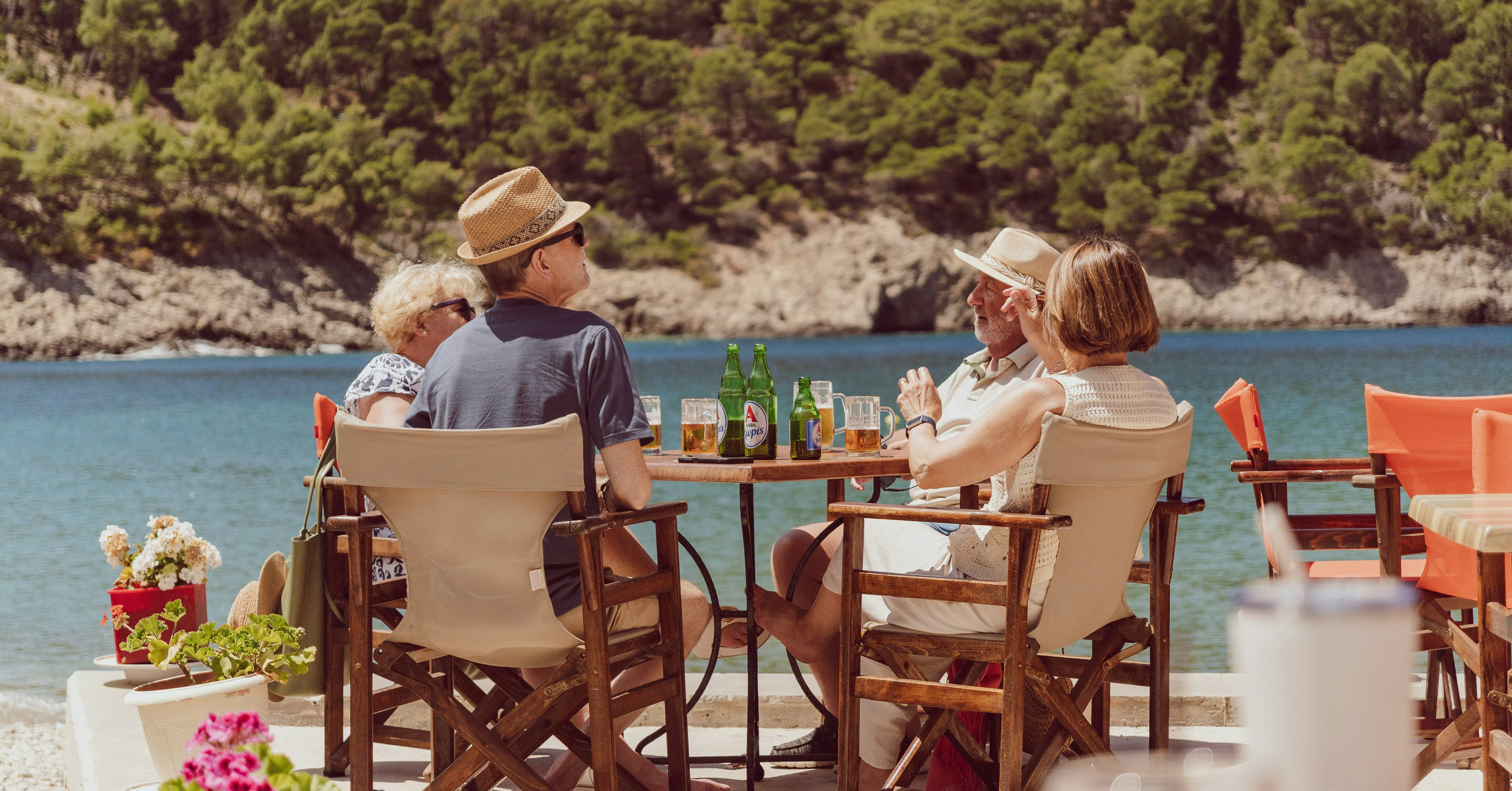 Two couples with cold drinks at a waterside café table above a turquoise cove