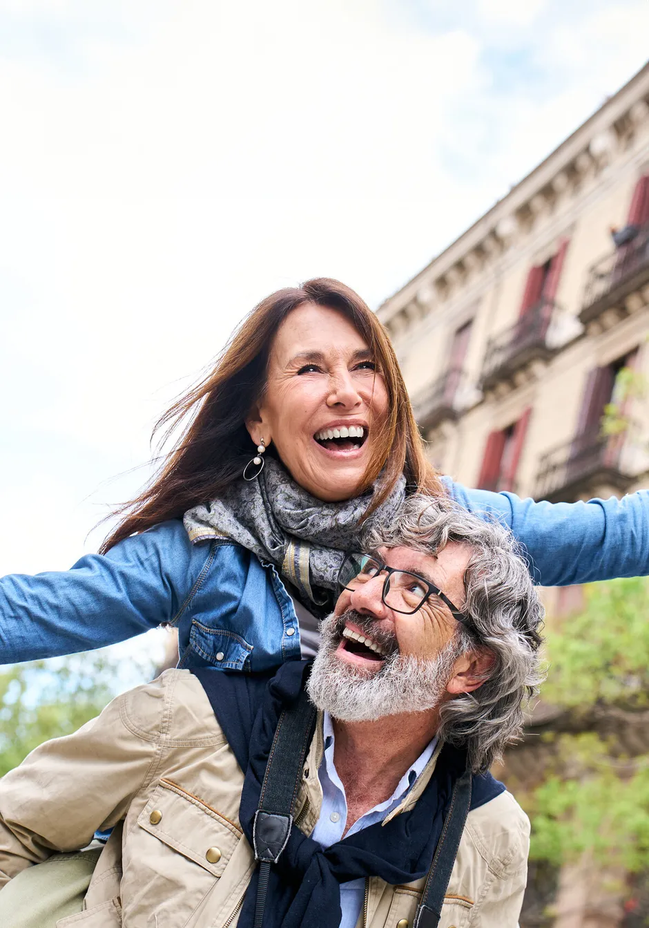 A laughing couple on a city street, one carrying the other piggyback